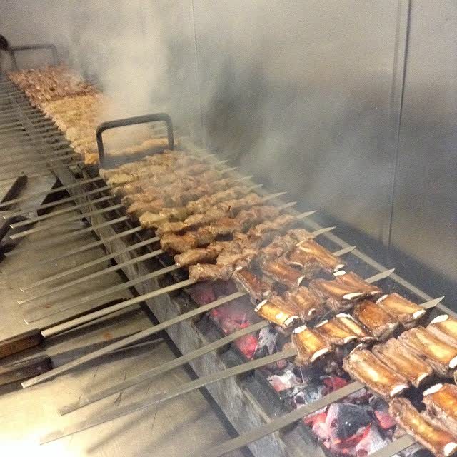 Skewers of meat over glowing coals in a steel trough